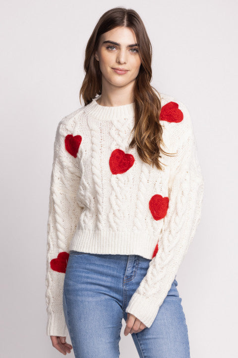 Spice up your wardrobe with the Pink Martini Delanie sweater. This cable knit white sweater features charming red hearts, giving your look a touch of love. Stay cozy and stylish with this playful addition to your winter collection.