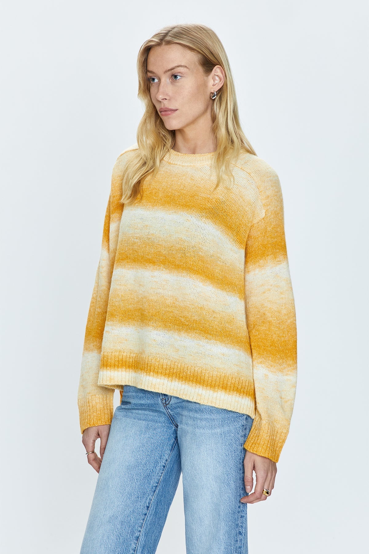 Lightweight transitional sweater crafted from a knit blend with a touch of wool. Crewneck silhouette with long sleeves, raglan shoulders, and a relaxed fit. Sunset is a dip-dye striped color effect featuring warm shades of ivory, yellow, and orange.