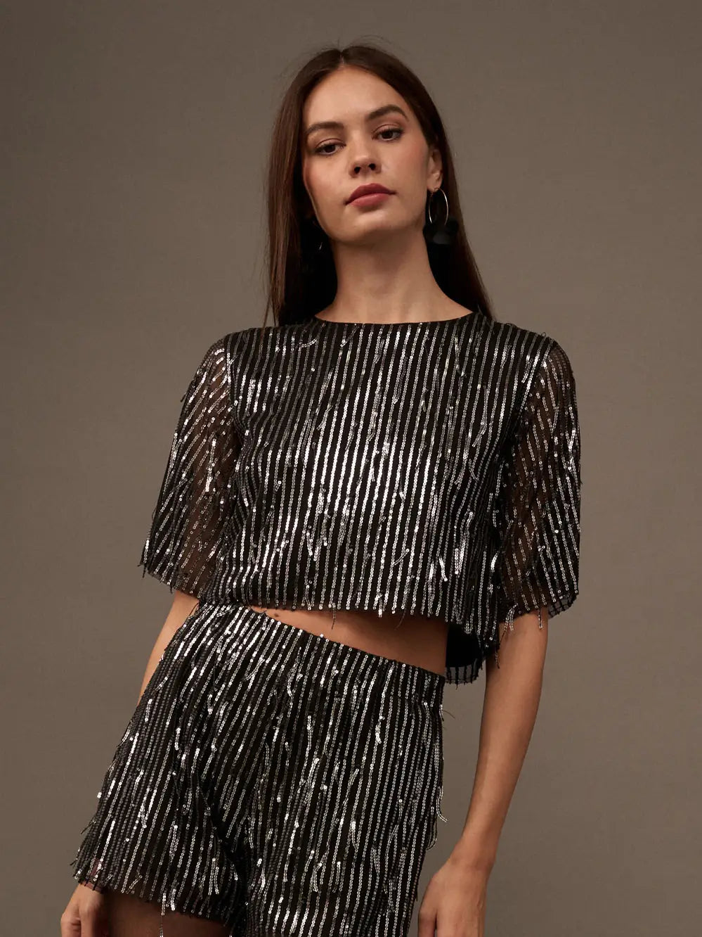 Shine bright with Promesa's Ogden crop top! Featuring a round-neck design, this long-sleeve top is adorned with stylish striped sequins. Show off your playful side with a touch of glam and pair it with high-waisted jeans for a fun and fashionable look.