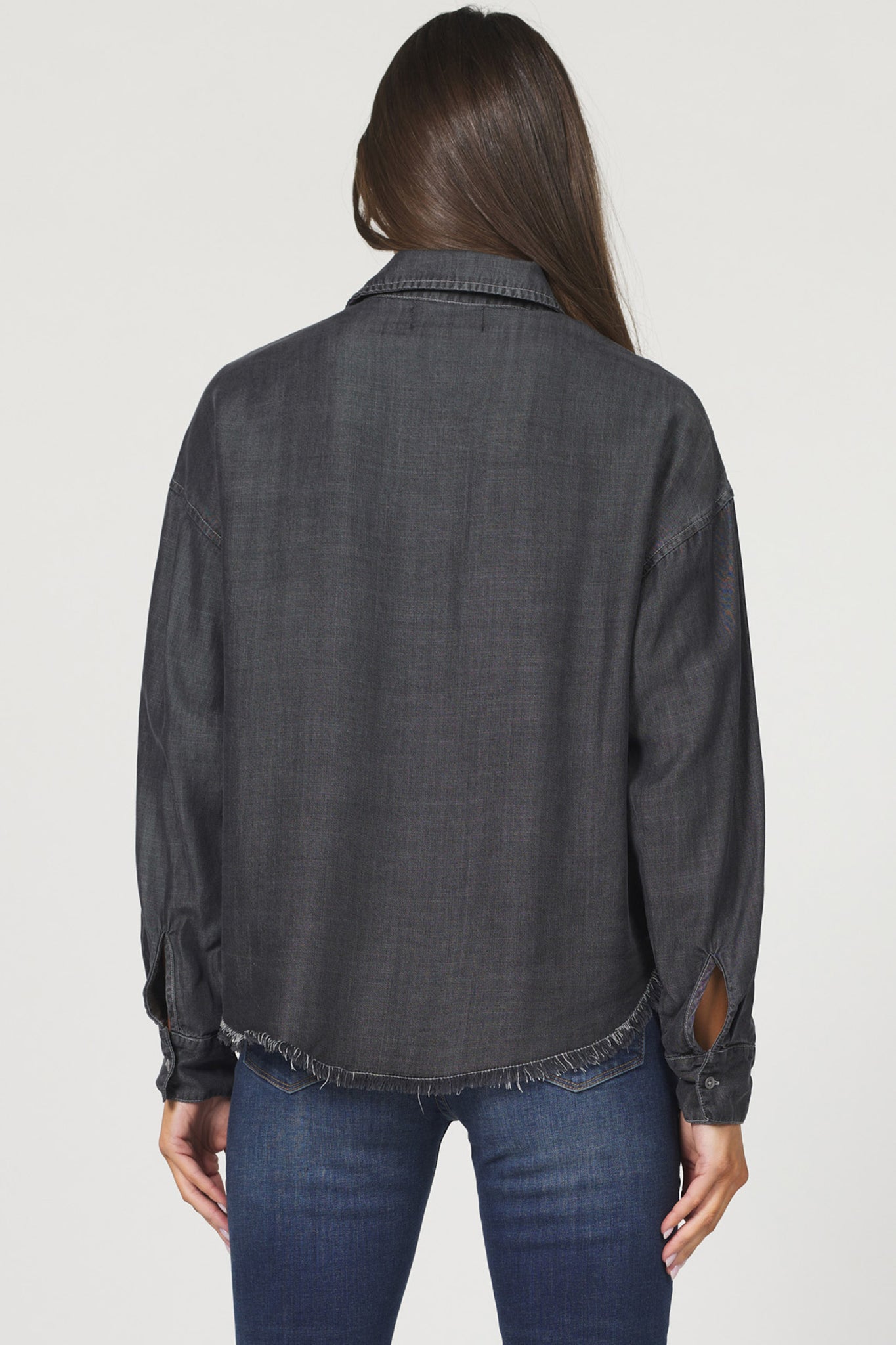 Person wearing a dark denim shirt with slight distressing on a plain background