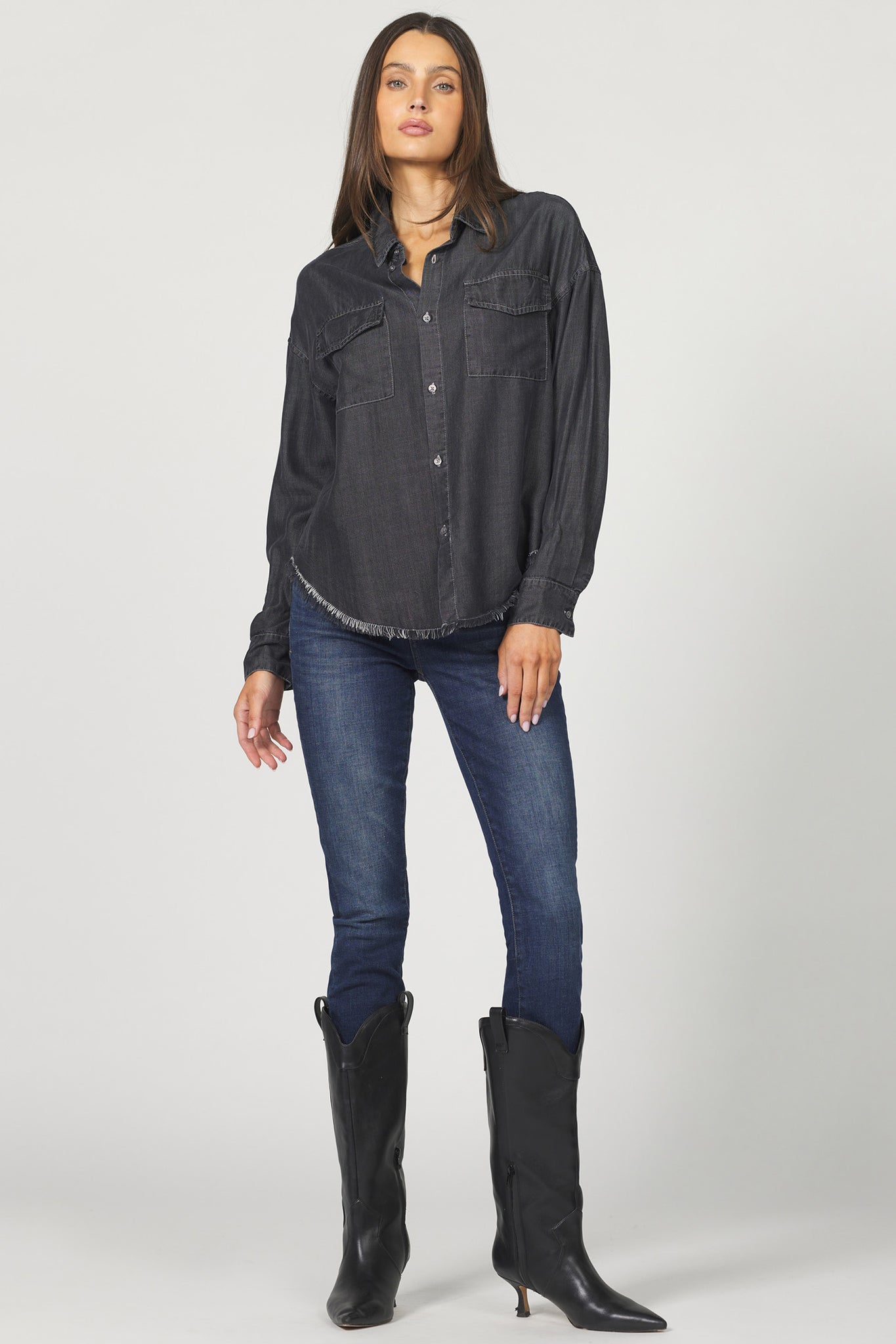 Woman wearing a dark denim shirt, blue jeans, and black boots on a white background