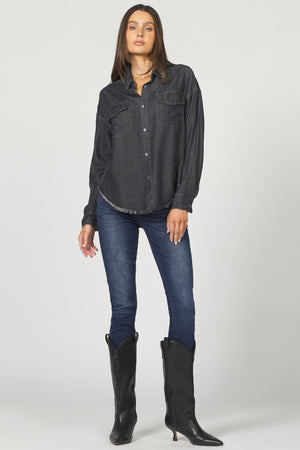 Woman wearing a dark denim shirt, blue jeans, and black boots on a white background
