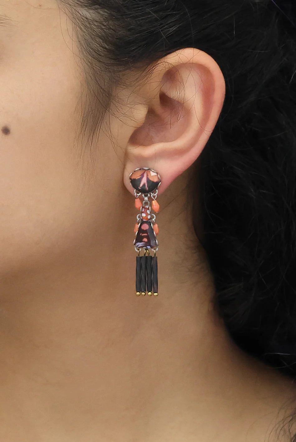Close-up of an ear wearing a decorative earring with black and red details.