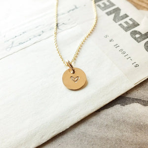 Gold necklace with a heart pendant on a marble surface