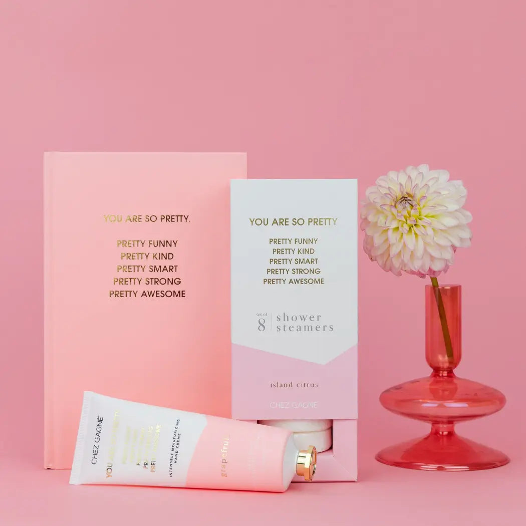 Product set with 'You are so pretty' cards, a tube of cream, and a flower on a pink background
