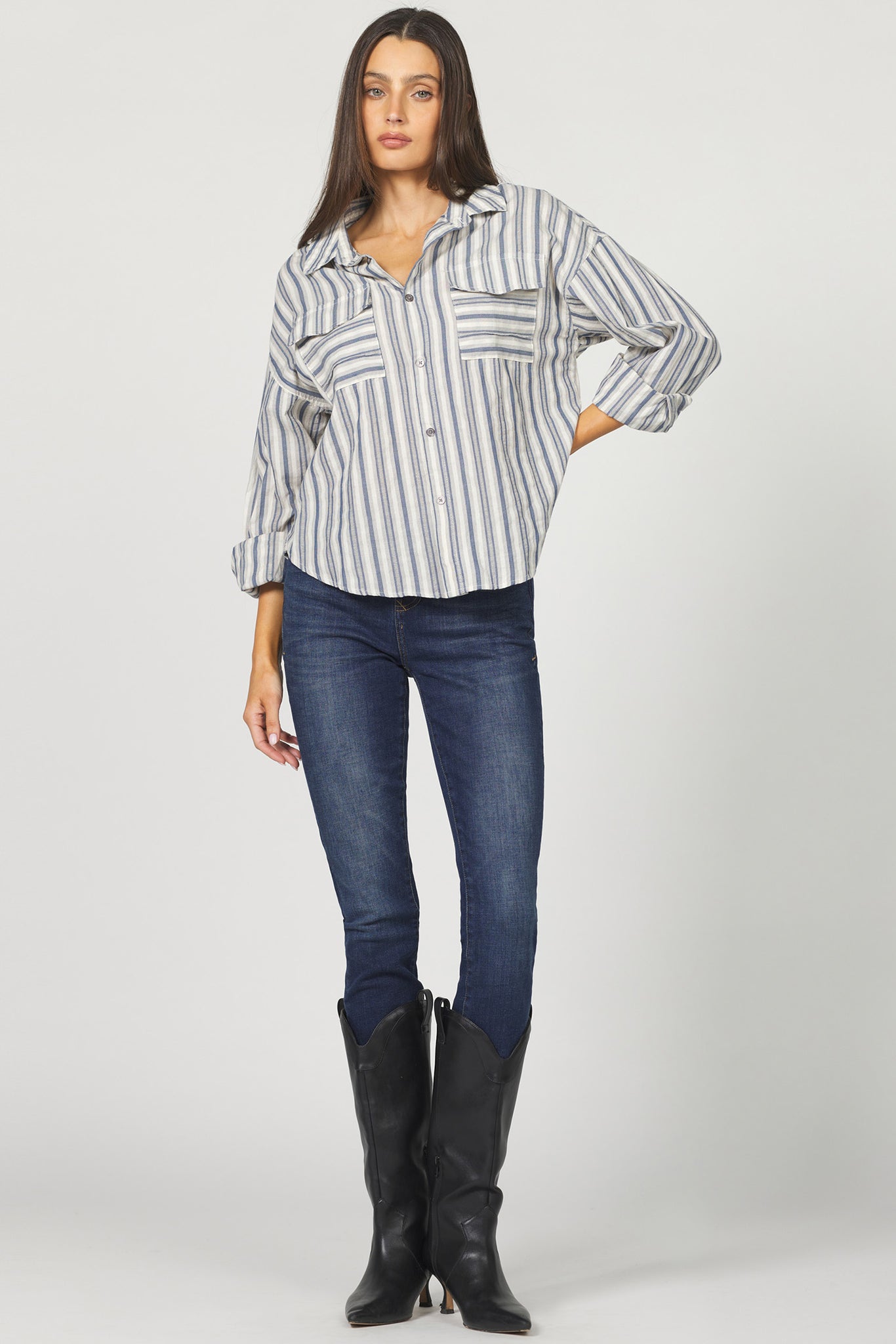 Woman wearing a striped shirt, blue jeans, and black boots on a white background