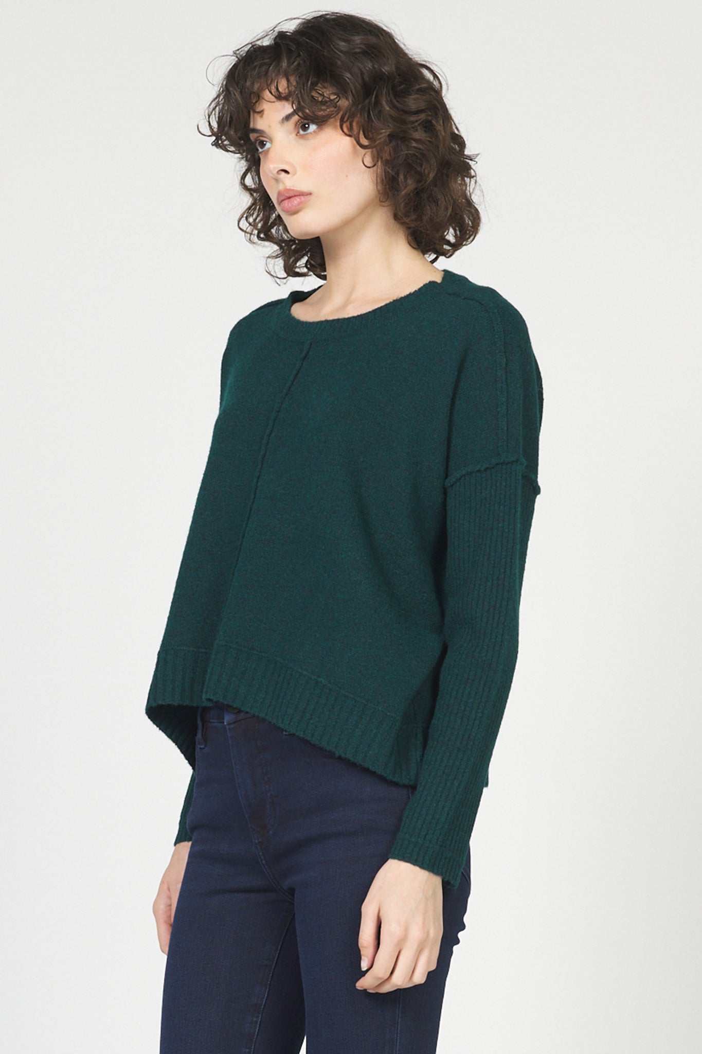 Woman wearing a green sweater and navy pants on a white background