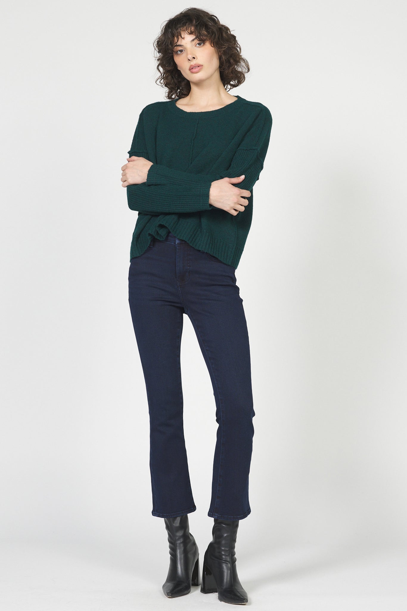 Woman wearing a green sweater and navy jeans on a white background