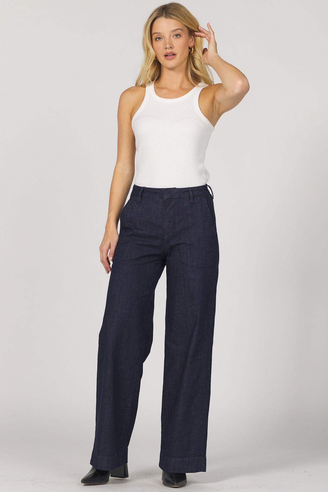 Woman wearing a white sleeveless top and navy pants on a plain background