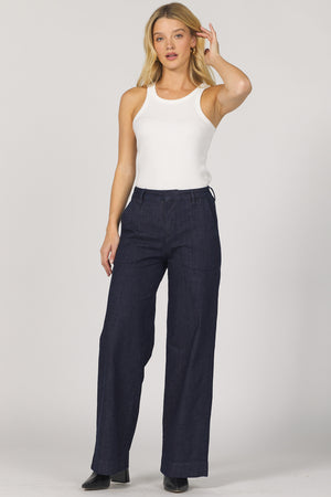 Woman wearing a white sleeveless top and navy pants on a plain background