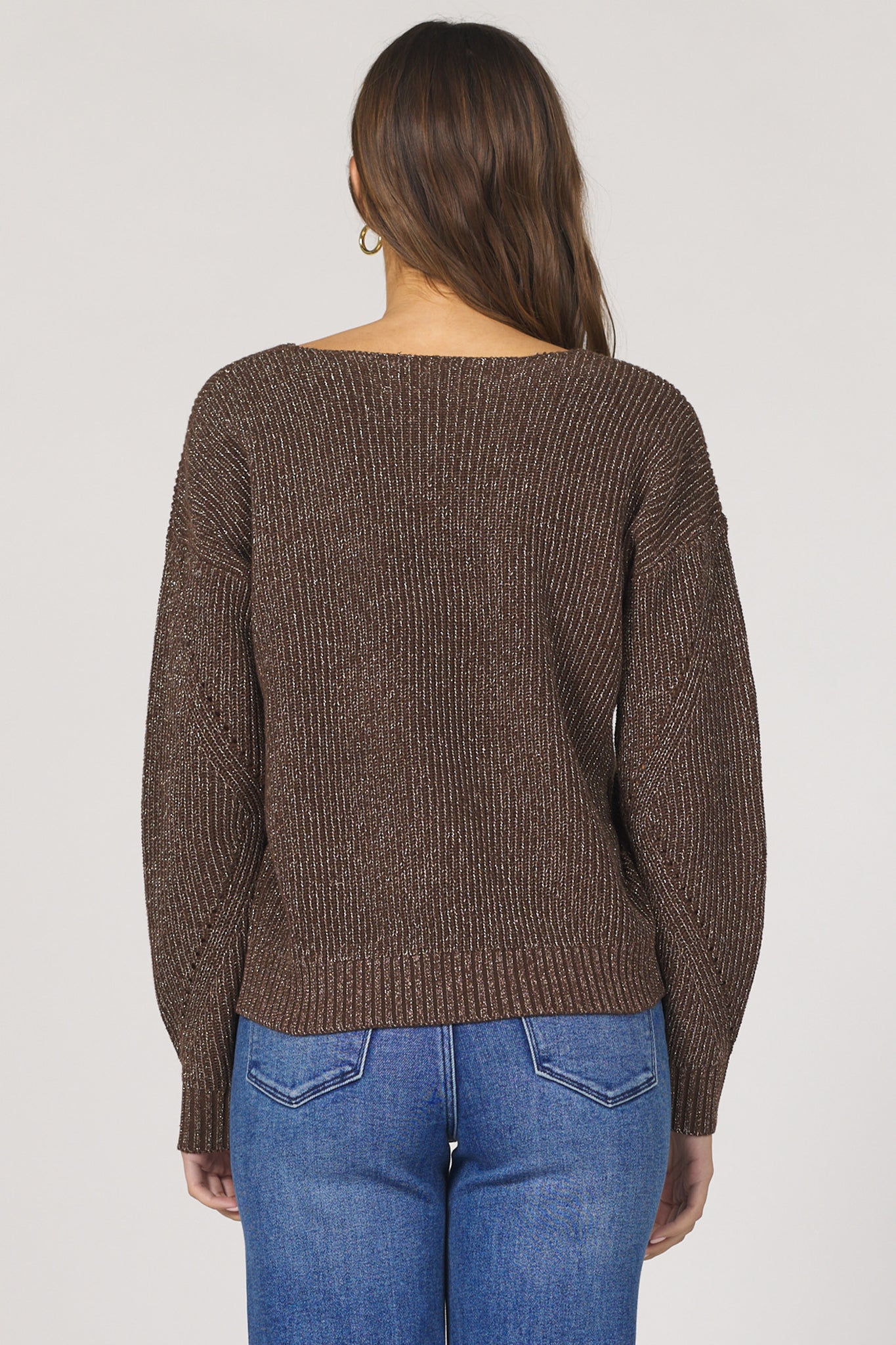 Person wearing a brown knitted sweater and blue jeans on a plain background