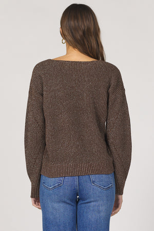 Person wearing a brown knitted sweater and blue jeans on a plain background