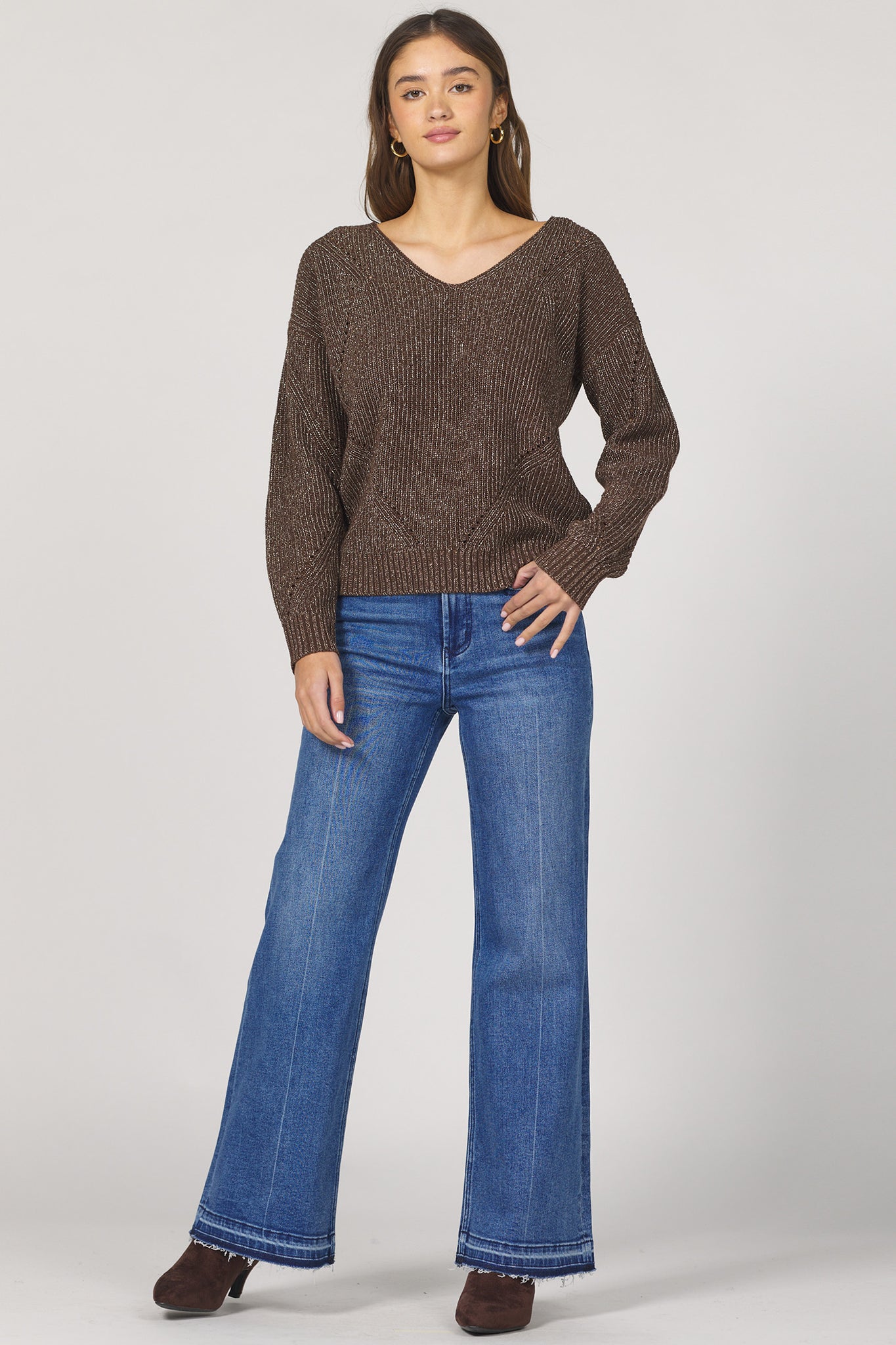 Woman wearing a brown sweater and blue jeans on a white background