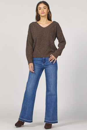 Woman wearing a brown sweater and blue jeans on a white background