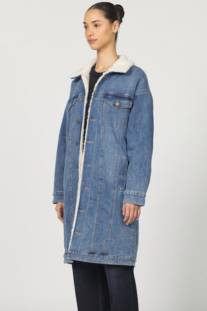 Woman wearing a blue denim coat with white fur lining on a white background