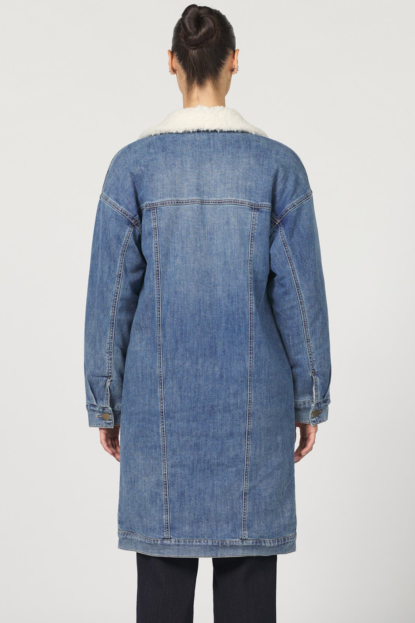 Person wearing a long denim coat on a white background