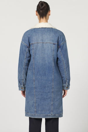 Person wearing a long denim coat on a white background