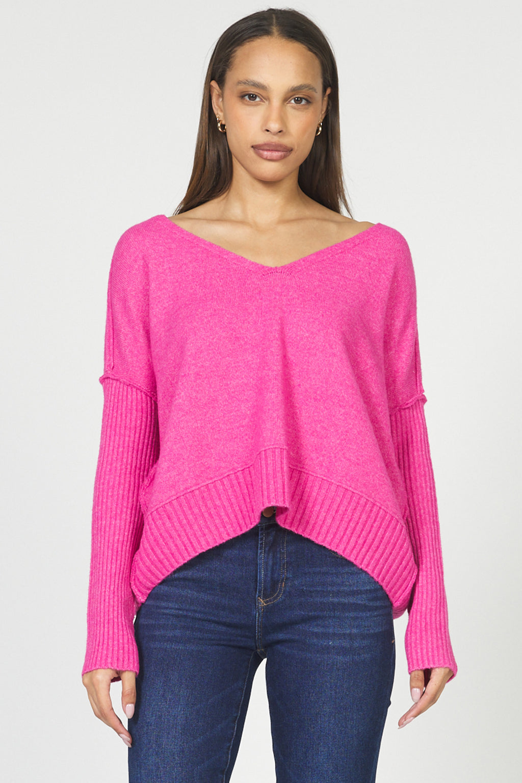 Woman wearing a bright pink sweater and blue jeans on a white background