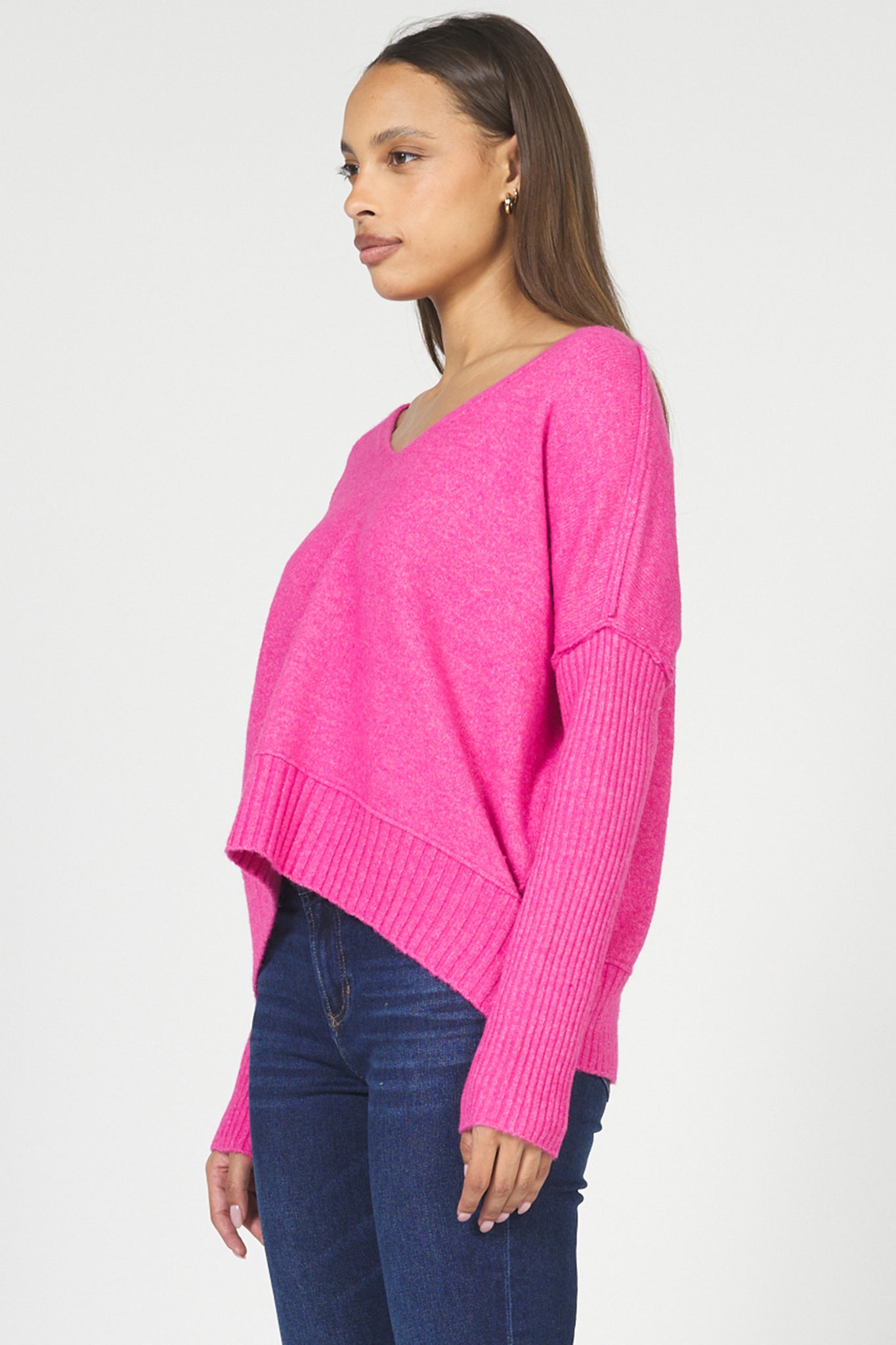 Woman wearing a bright pink sweater and blue jeans on a white background