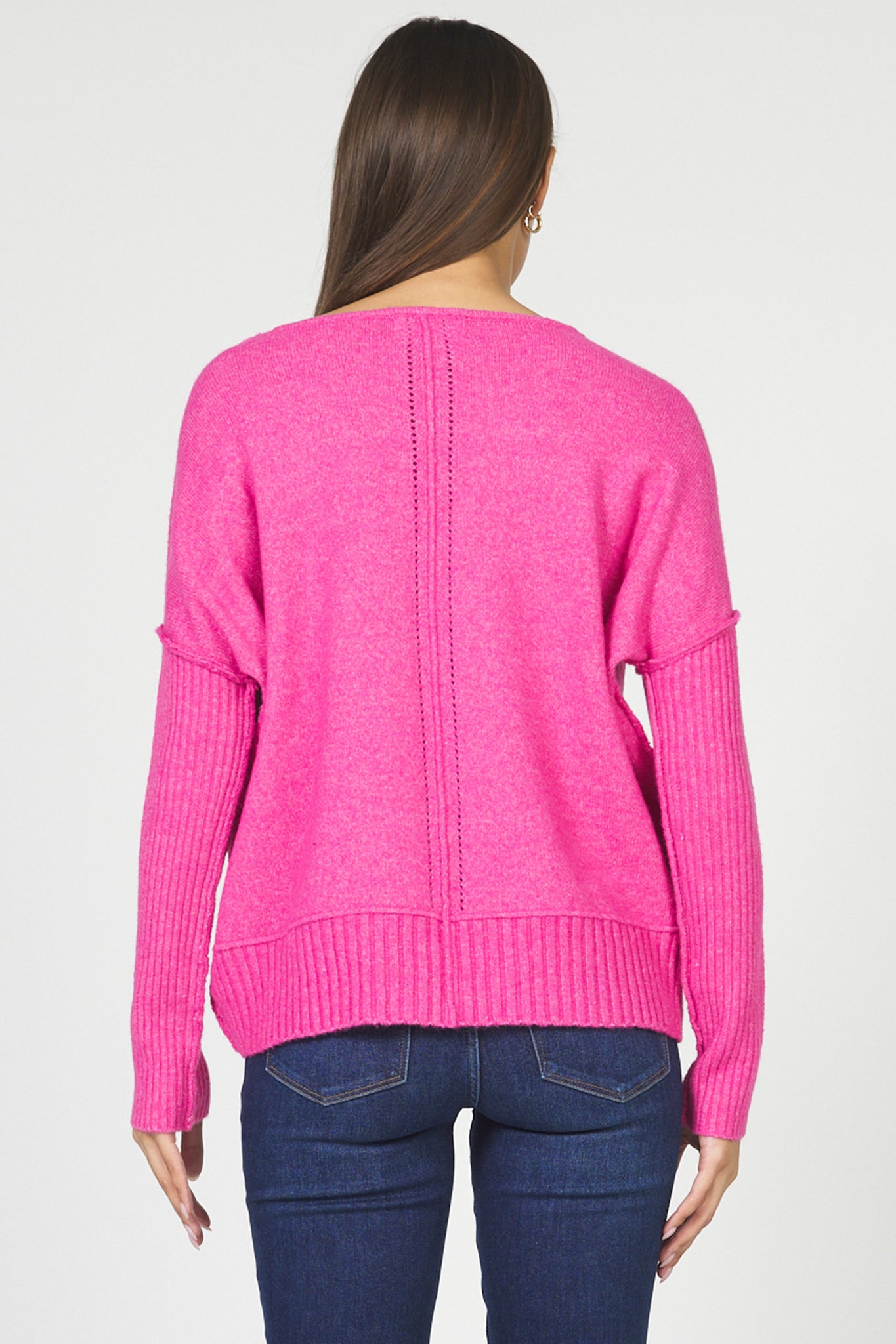 Person wearing a bright pink sweater and blue jeans on a white background