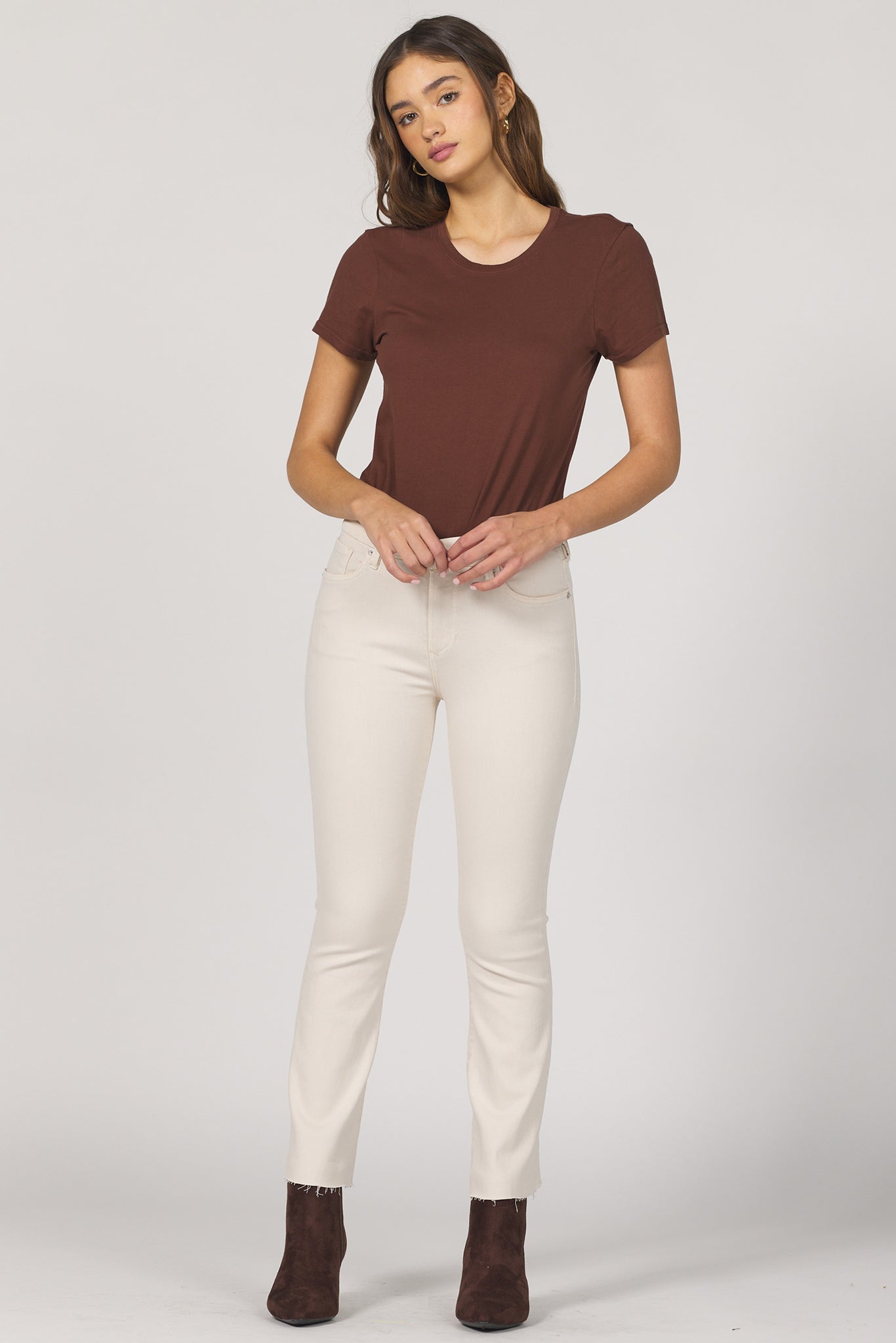 Woman wearing a brown t-shirt and white pants on a plain background