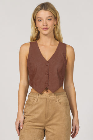 Woman wearing a brown vest over a beige top with a plain background