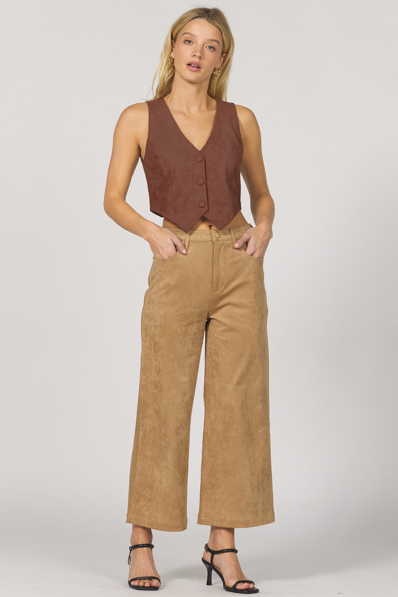 Woman wearing a brown vest and tan pants on a white background