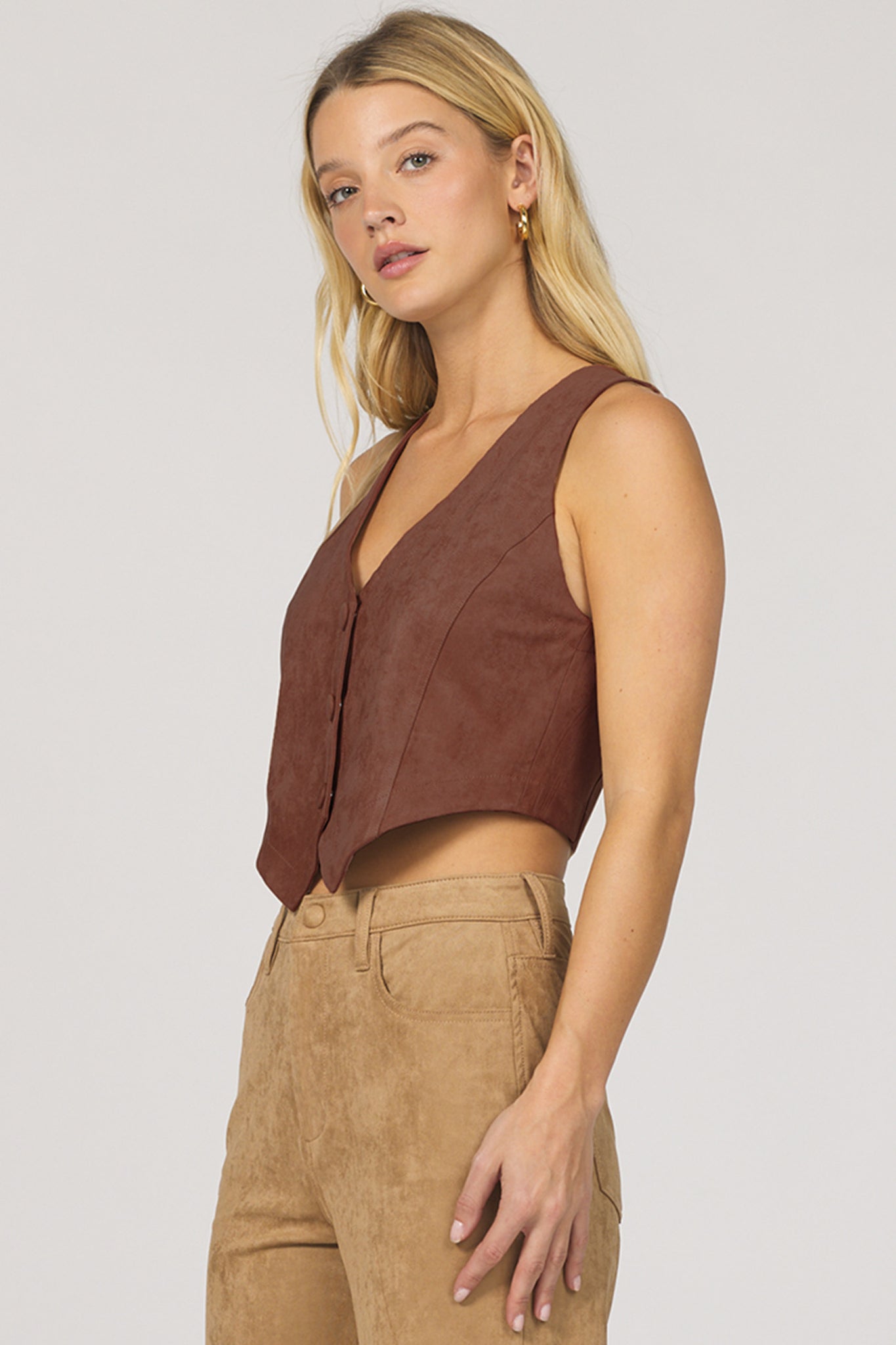Woman wearing a brown sleeveless top and beige pants on a plain background