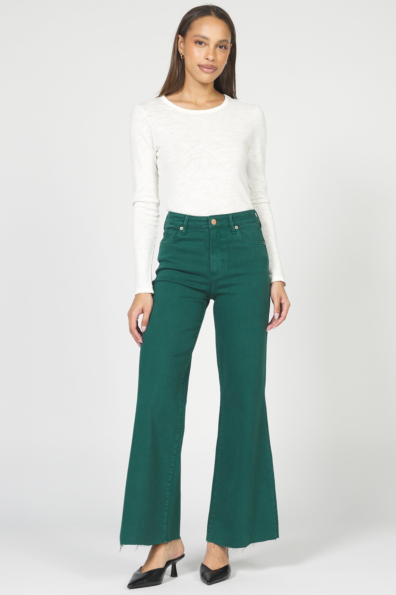 Woman wearing a white long-sleeve top and green high-waisted pants on a white background