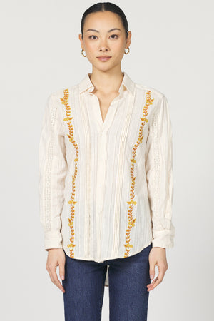 Woman wearing a cream blouse with gold embroidery on a white background