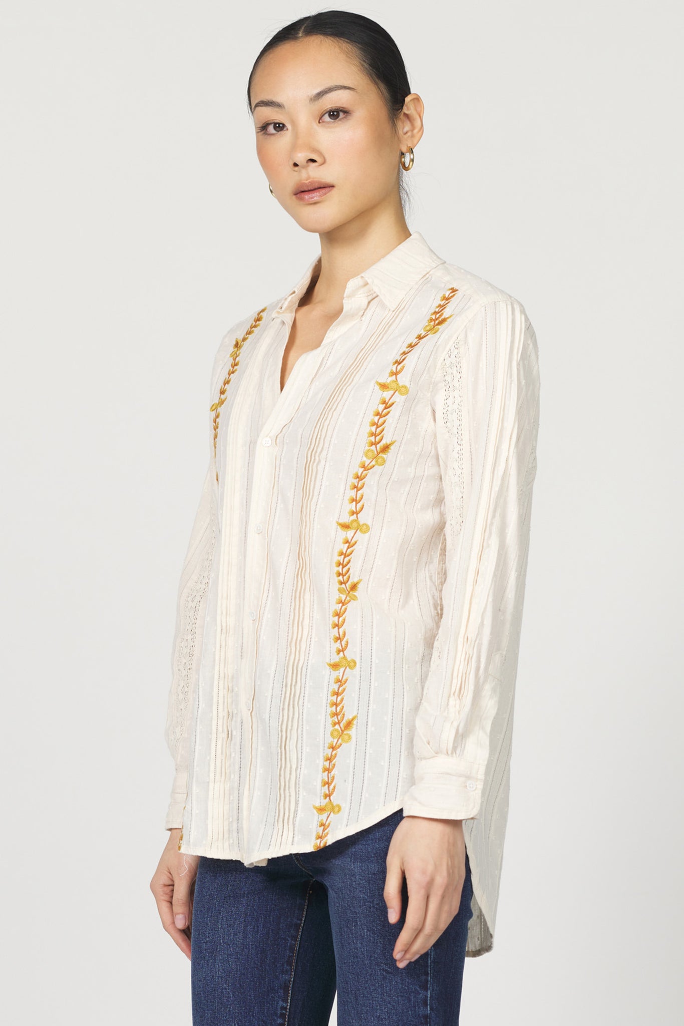 Woman wearing a white blouse with gold embroidery on a plain background