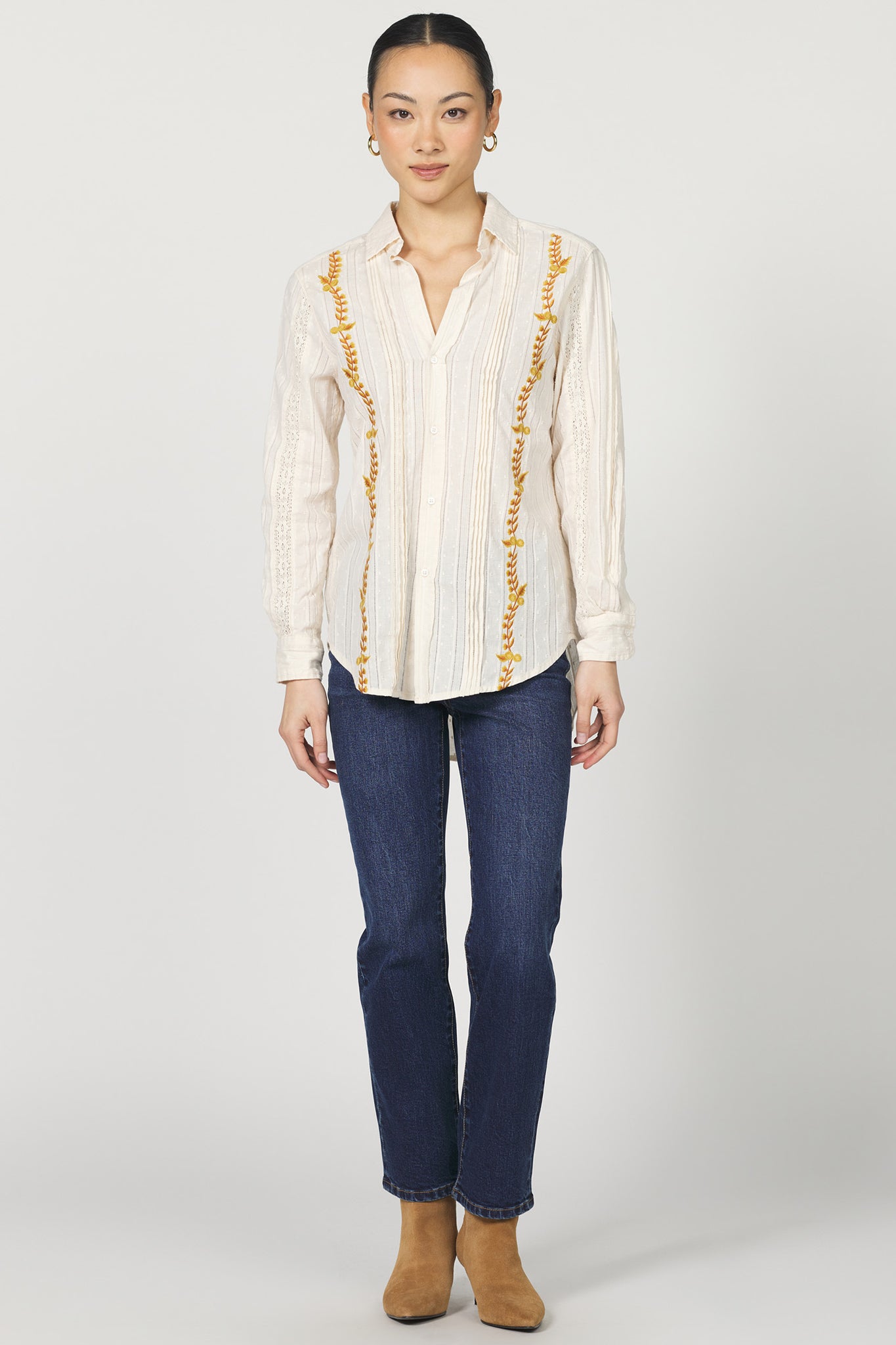 Woman wearing a white blouse with yellow accents and blue jeans on a white background