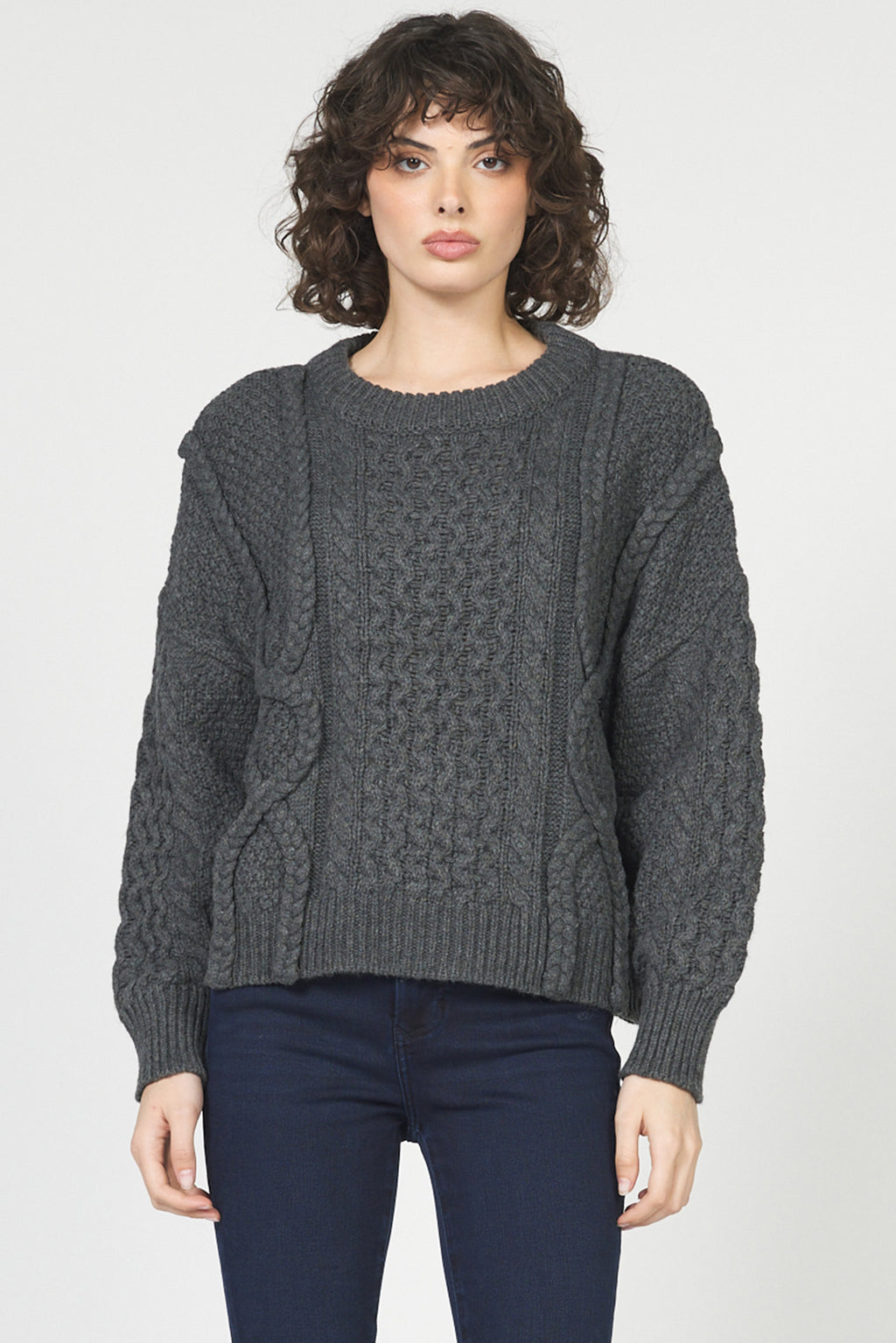 Woman wearing a gray cable knit sweater against a plain background