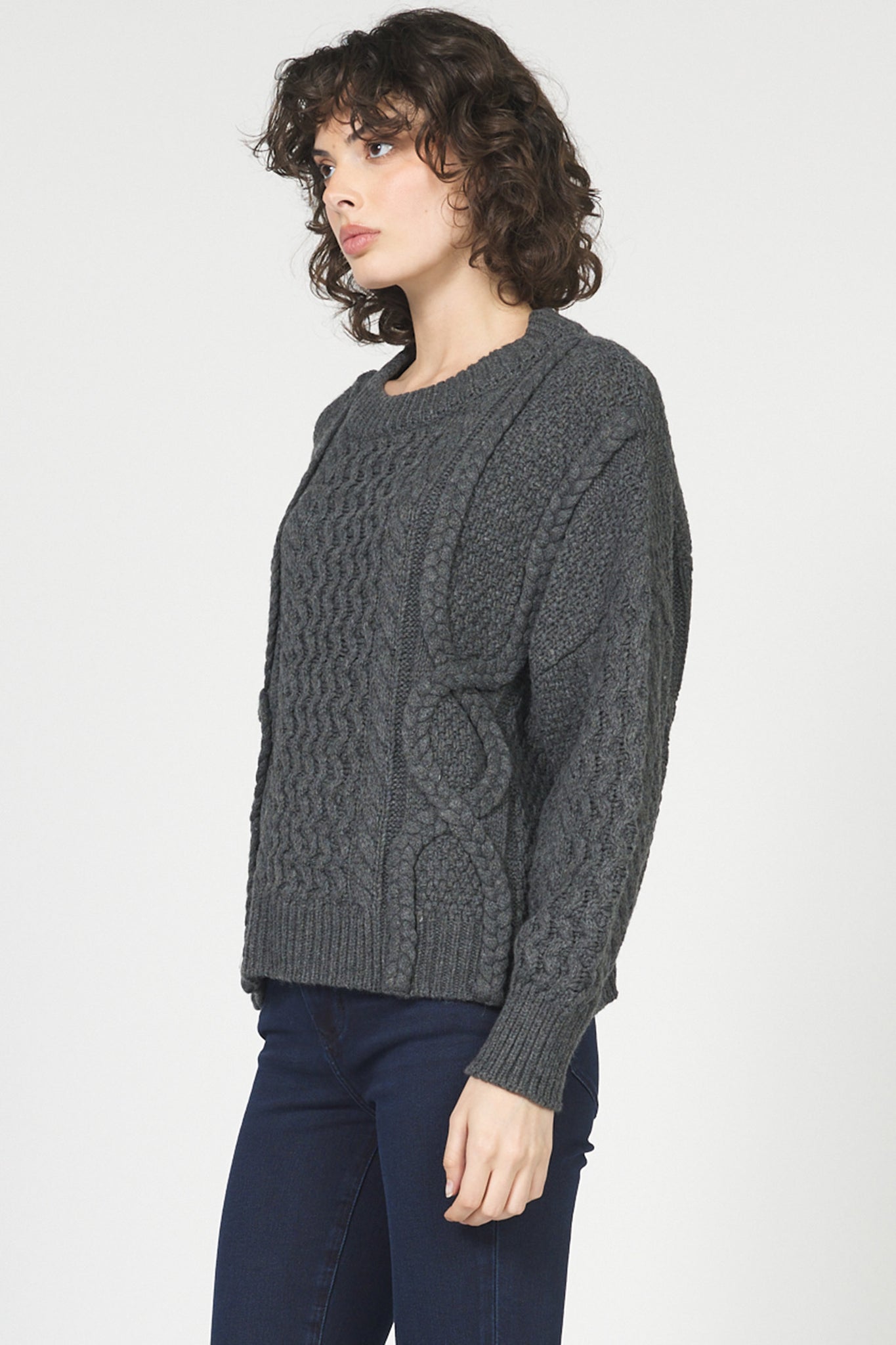 Woman wearing a gray cable knit sweater against a white background