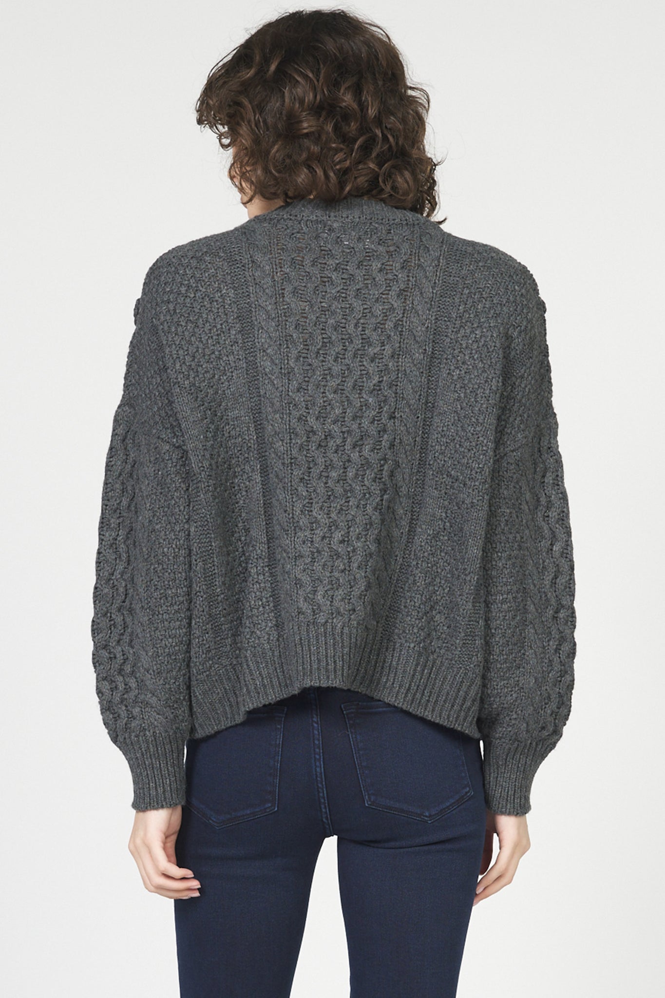 Person wearing a gray cable knit sweater on a white background