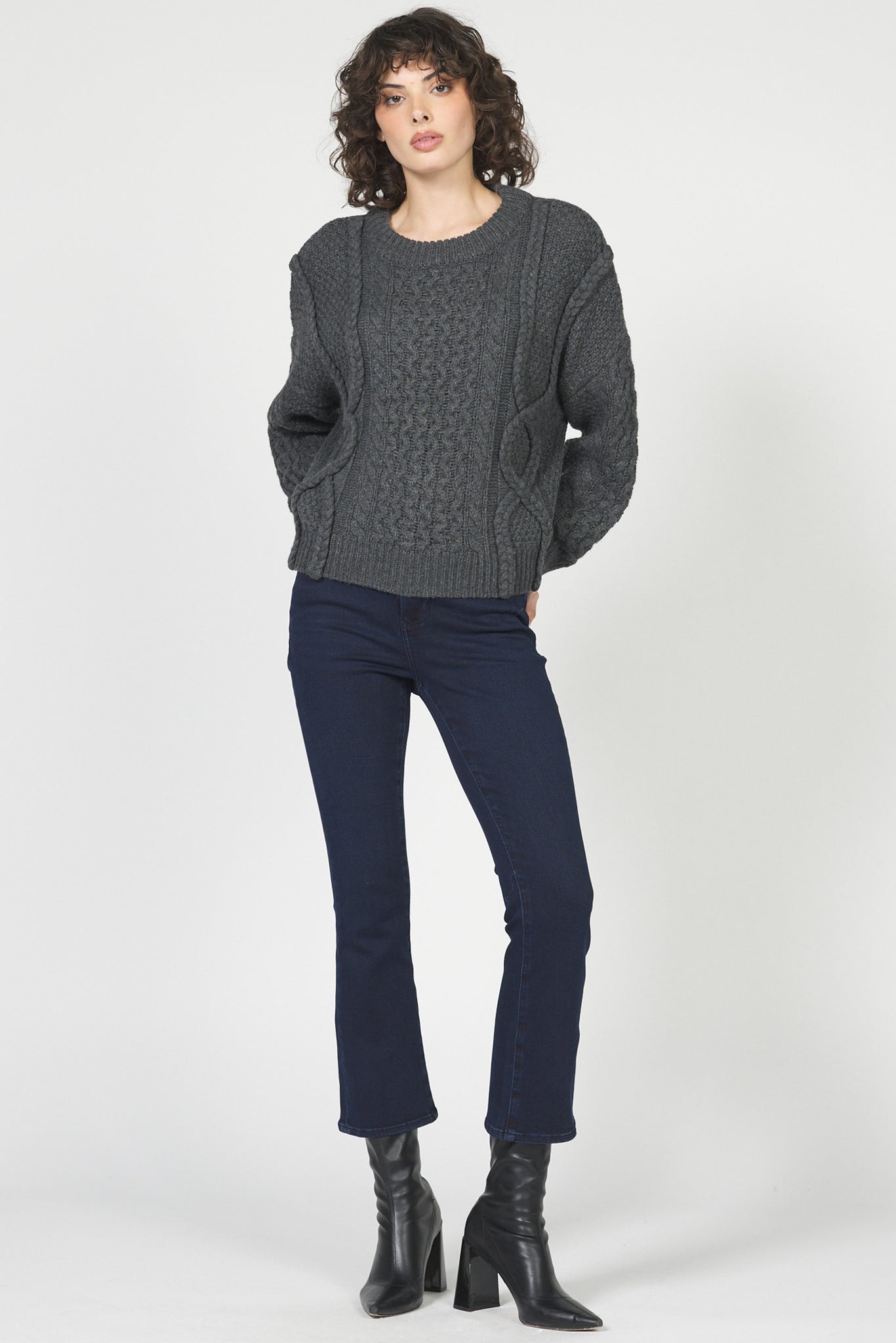 Woman wearing a gray cable knit sweater and navy jeans on a white background
