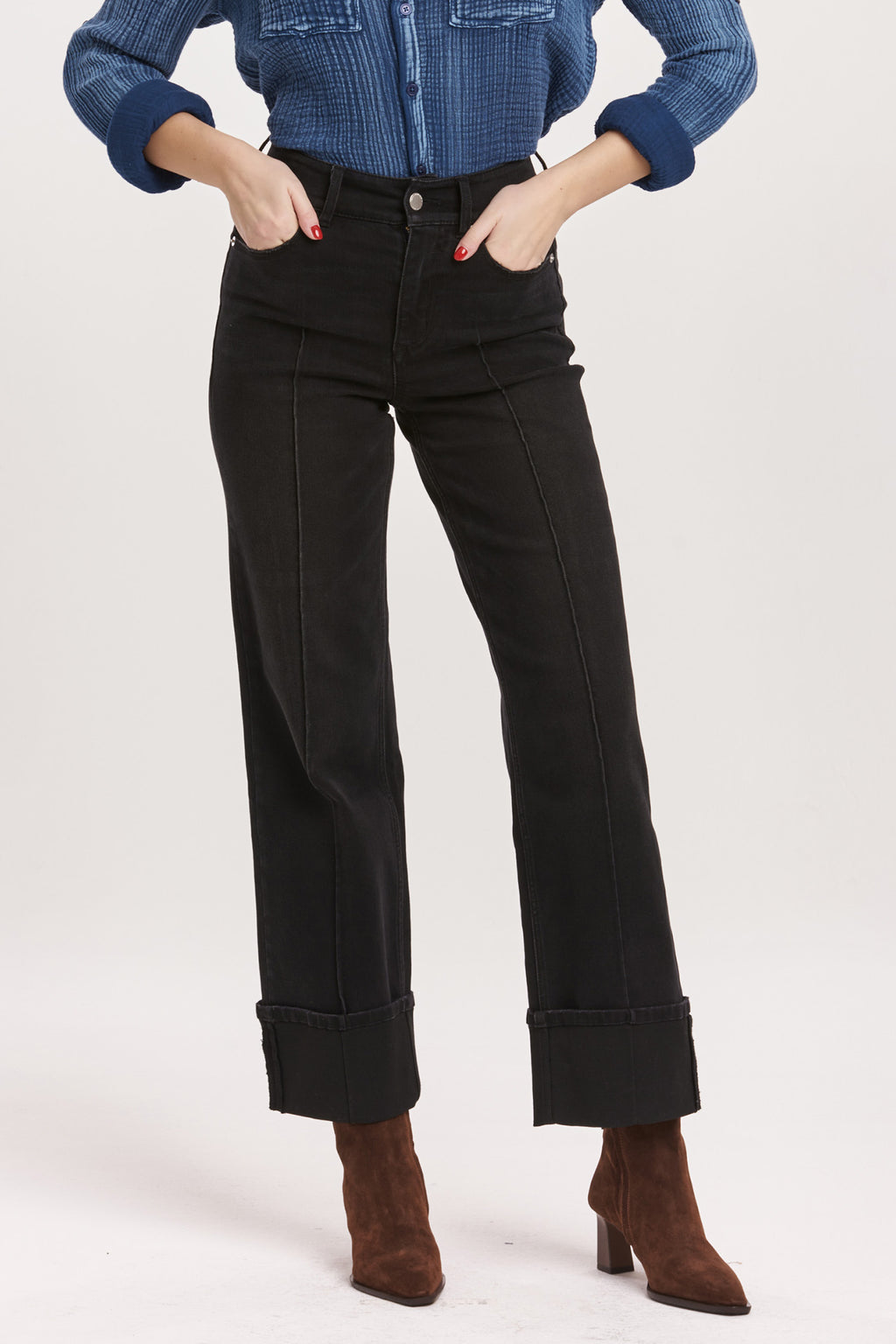 Person wearing black jeans with a blue denim shirt on a white background
