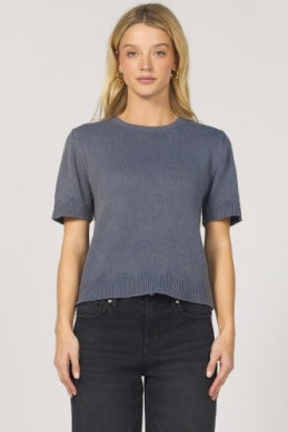 Woman wearing a blue sweater and black pants on a light gray background