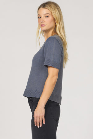 Woman wearing a gray knit top and black pants on a plain background