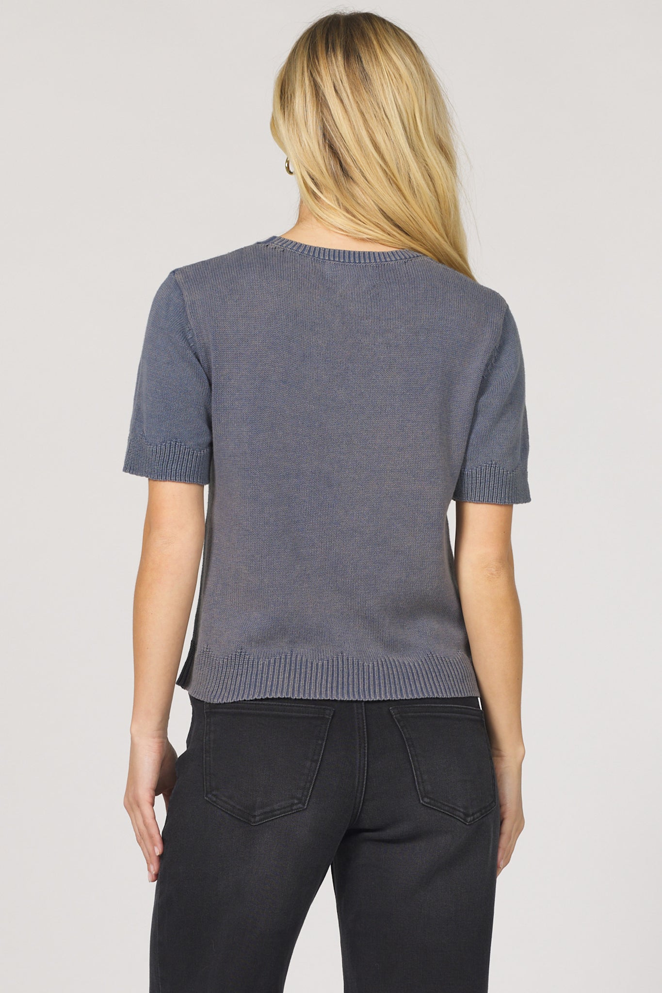 Person wearing a gray short-sleeve sweater and black pants on a plain background