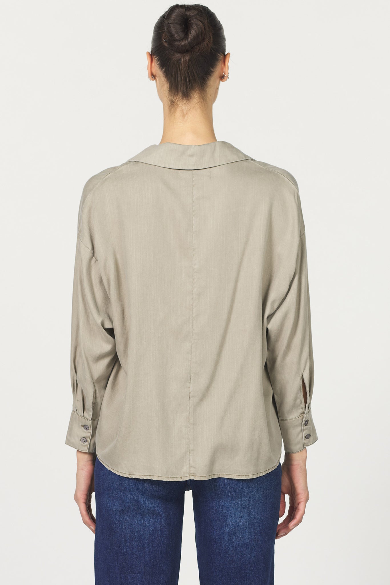 Person wearing a beige shirt and blue jeans on a white background