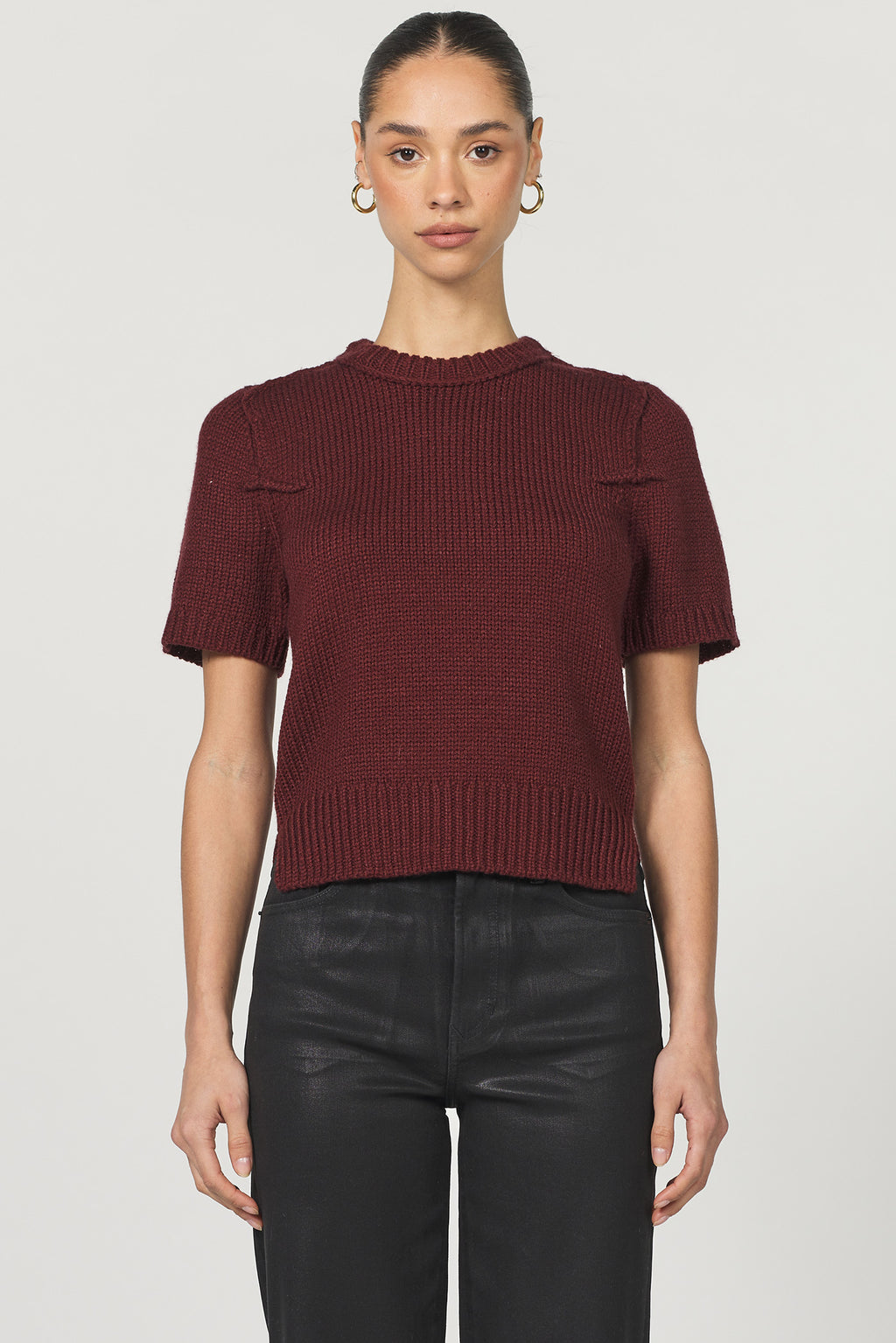 Person wearing a burgundy short-sleeve knit top and black pants on a light gray background