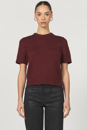 Person wearing a burgundy short-sleeve knit top and black pants on a light gray background