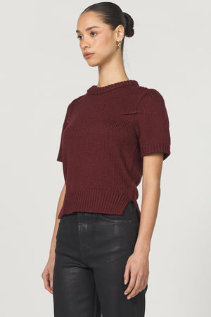Woman wearing a burgundy short-sleeve sweater and black pants on a light gray background