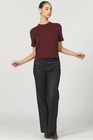 Woman wearing a burgundy sweater and black pants on a white background