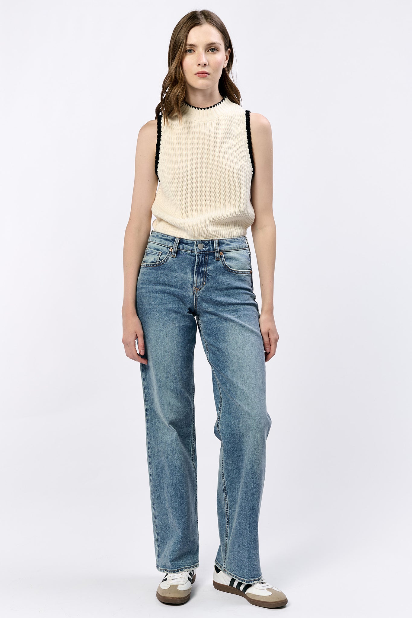 Woman wearing a cream sleeveless top and blue jeans on a white background
