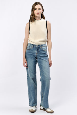 Woman wearing a cream sleeveless top and blue jeans on a white background