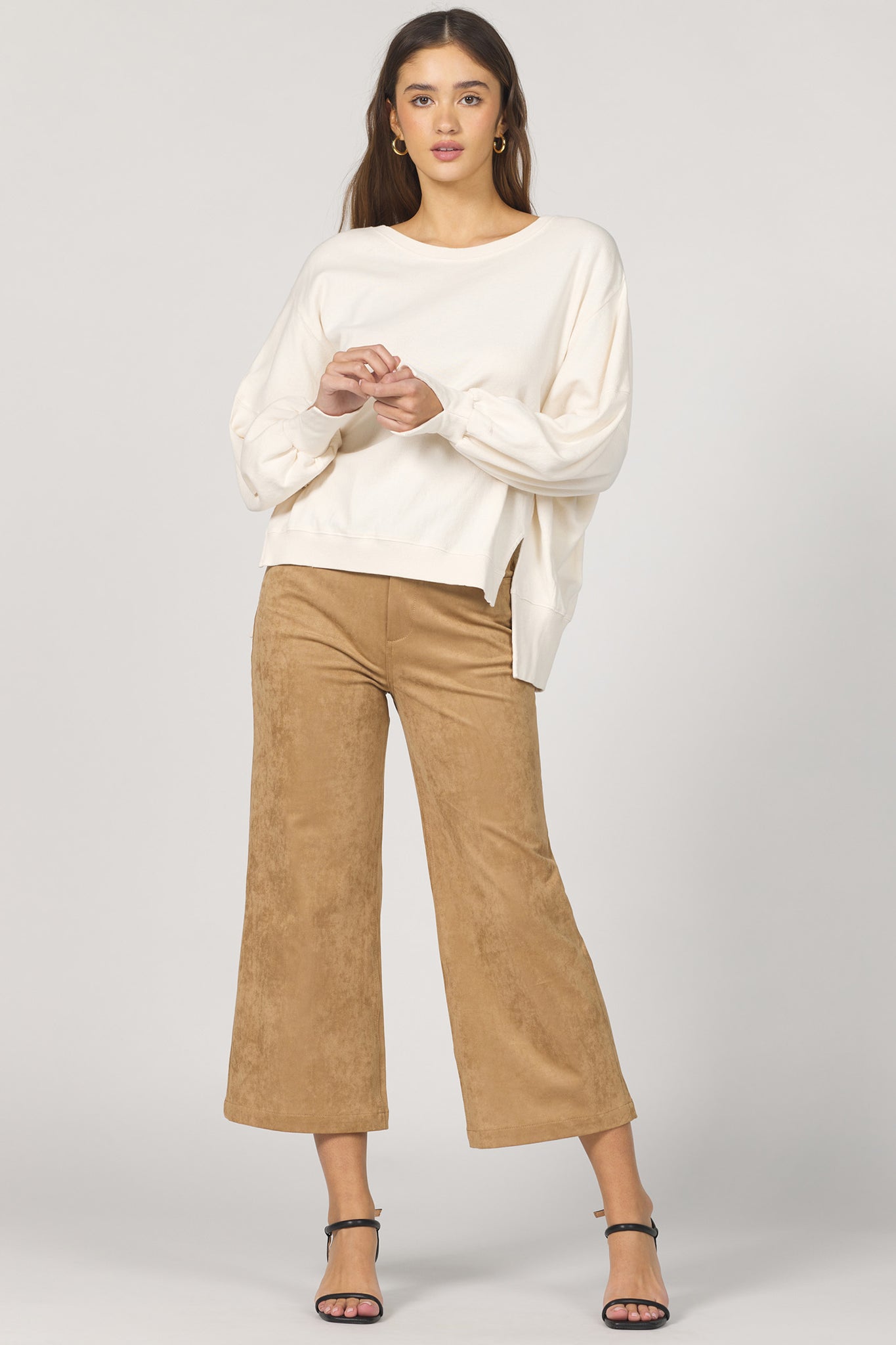 Woman wearing a white sweater and brown pants on a plain background