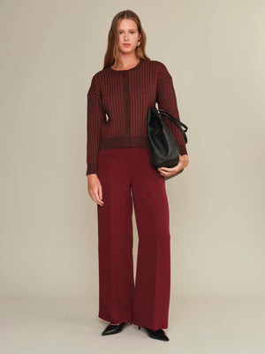Woman wearing a burgundy outfit with a black bag on a beige background