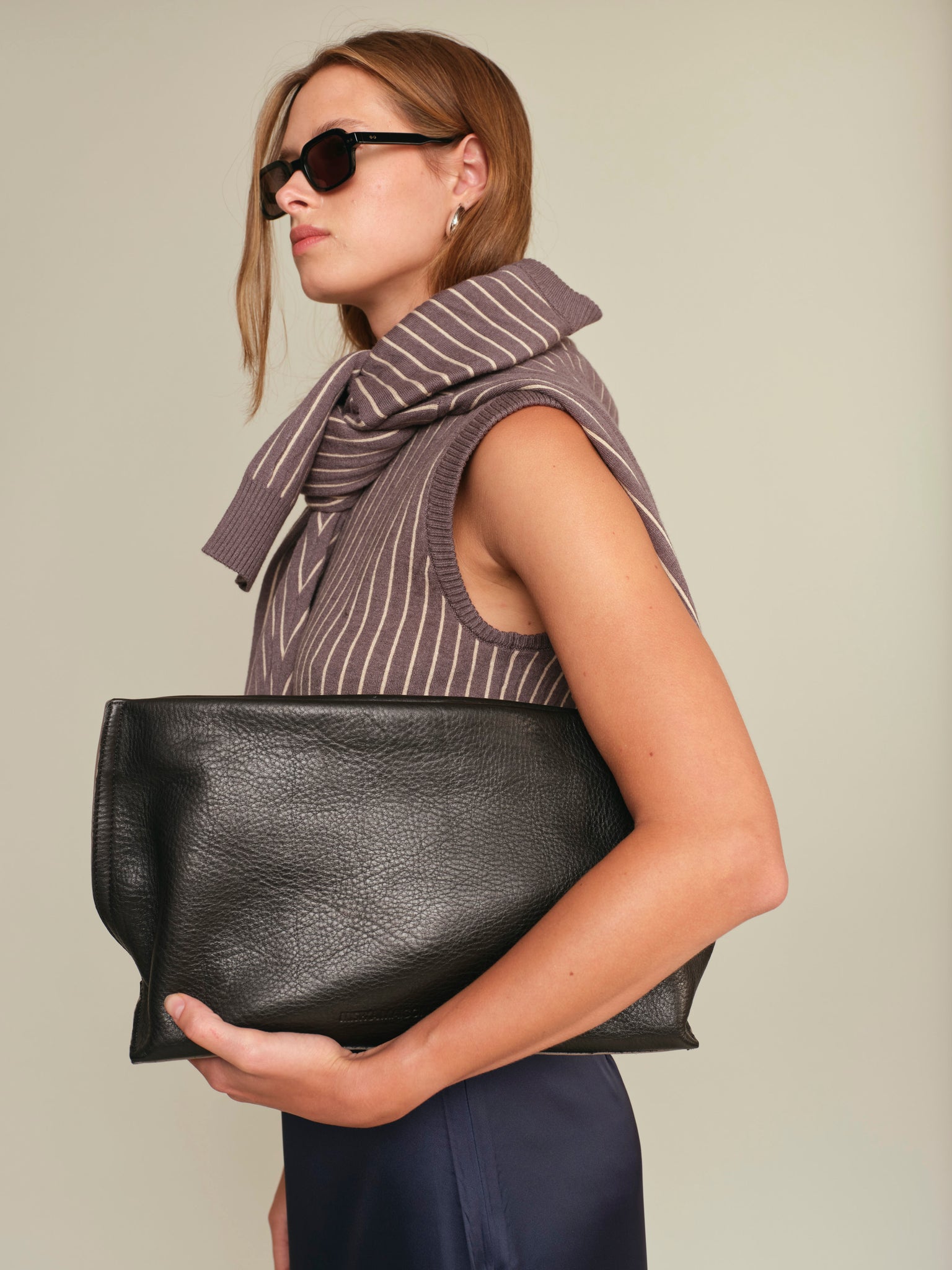 Woman holding a black clutch bag against a neutral background